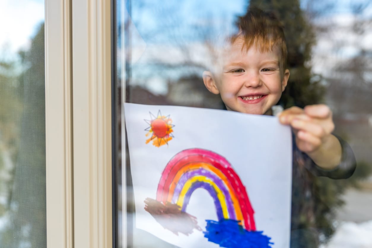 coronavirus kid holding rainbow picture up inside window