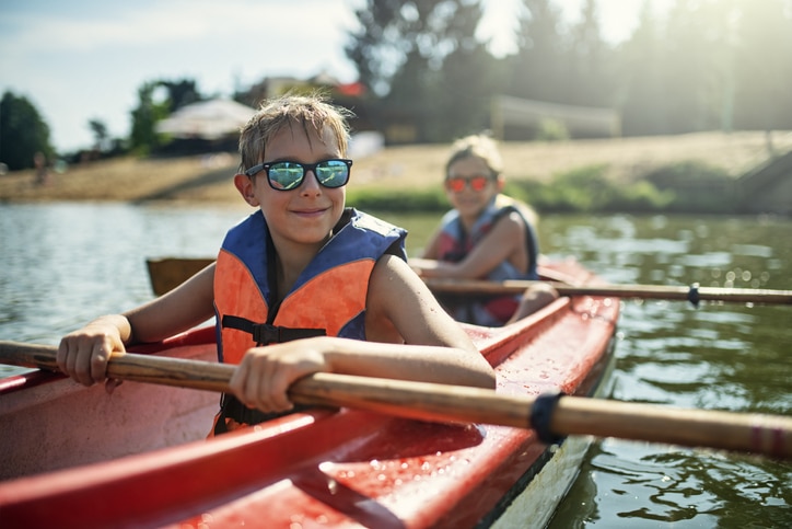 Two boys enjoying kayaking on lake on sunny summer day