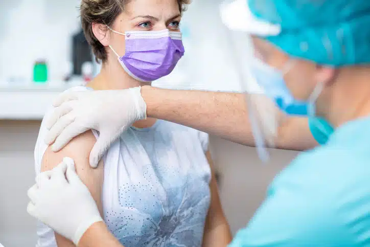 Female patient with protective face mask waiting for vaccination, doctor in surgical gloves disinfecting her arm