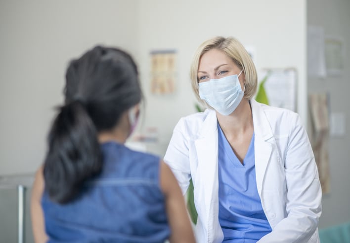 7 year old female patient speaking with her paediatrician in a doctors office, both are wearing masks due to the new COVID-19 regulations and to avoid the transfer of germs.