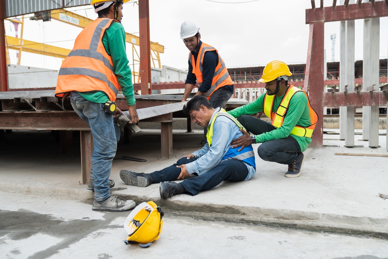 Men working and a man with workers compensation injuries on the ground