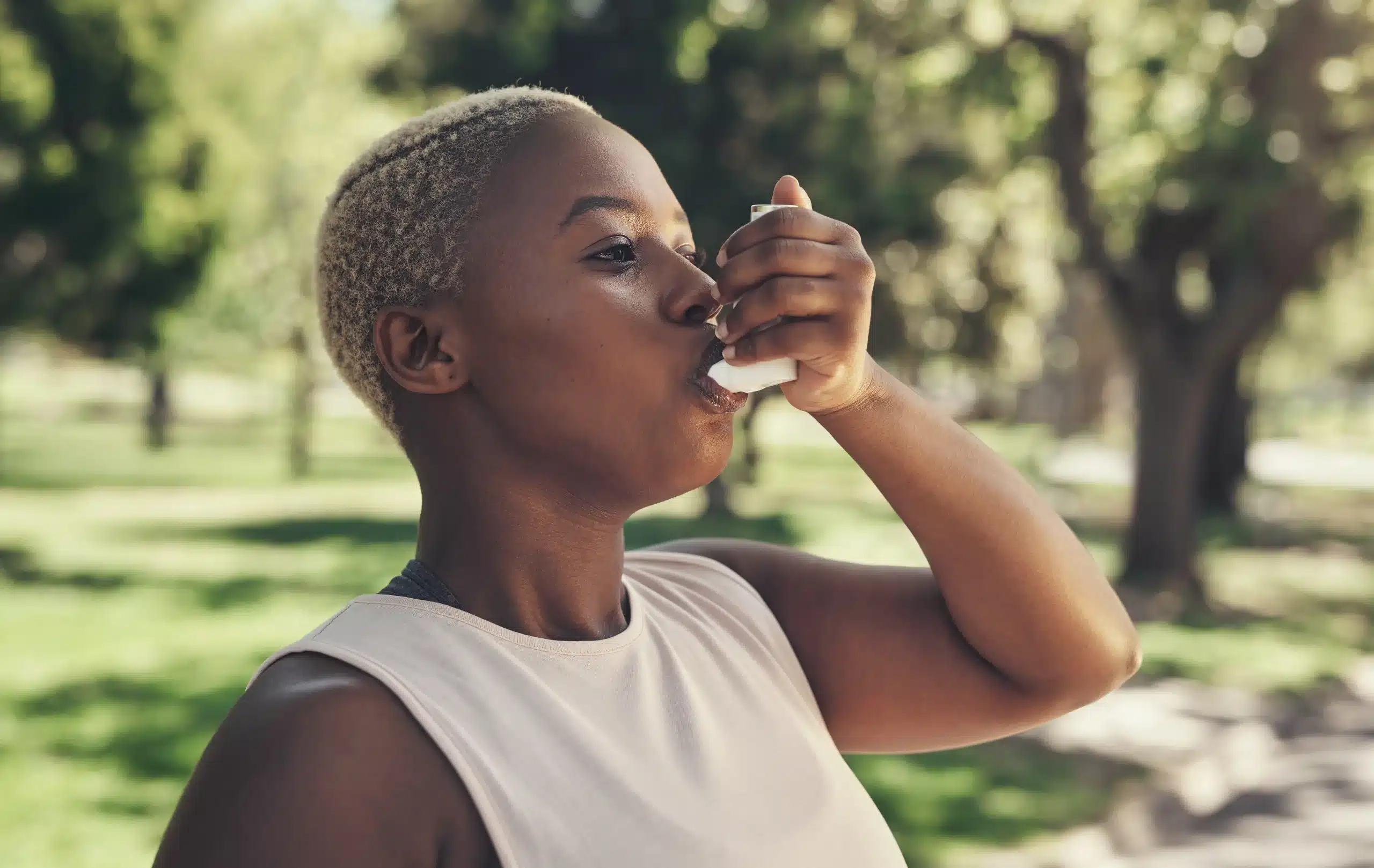 Black woman uses asthma inhaler after exercising outside.